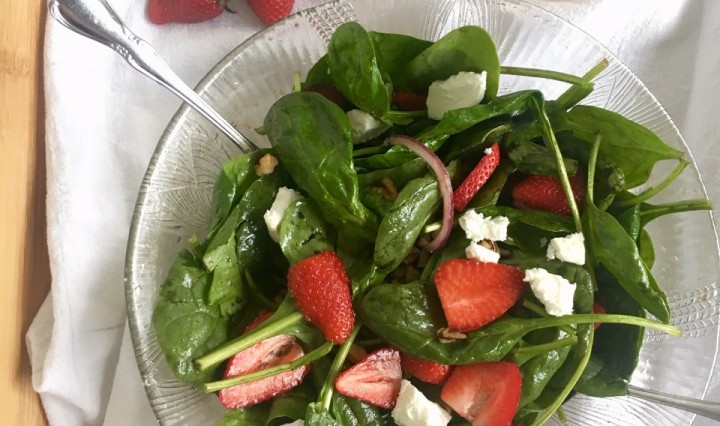 A large glass salad bowl filled with strawberry and spinach salad. Vinaigrette in a jar on the side.