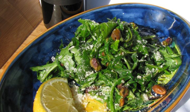 Wilted arugula salad in an oval blue bowl.