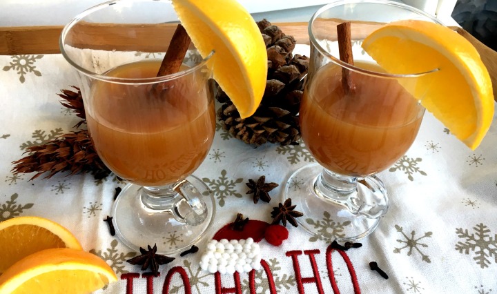 Two glasses of spiced apple cider with orange wedges and cinnamon sticks.