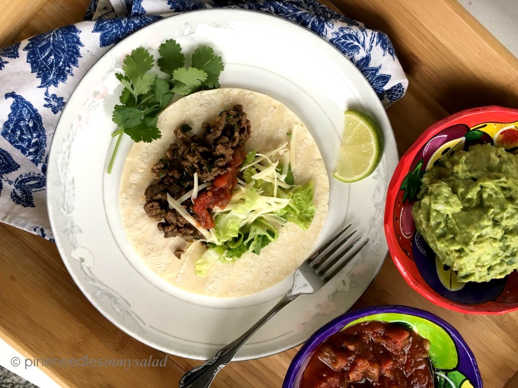 A plate with ground beef tacos. Salsa and guacamole on the side.