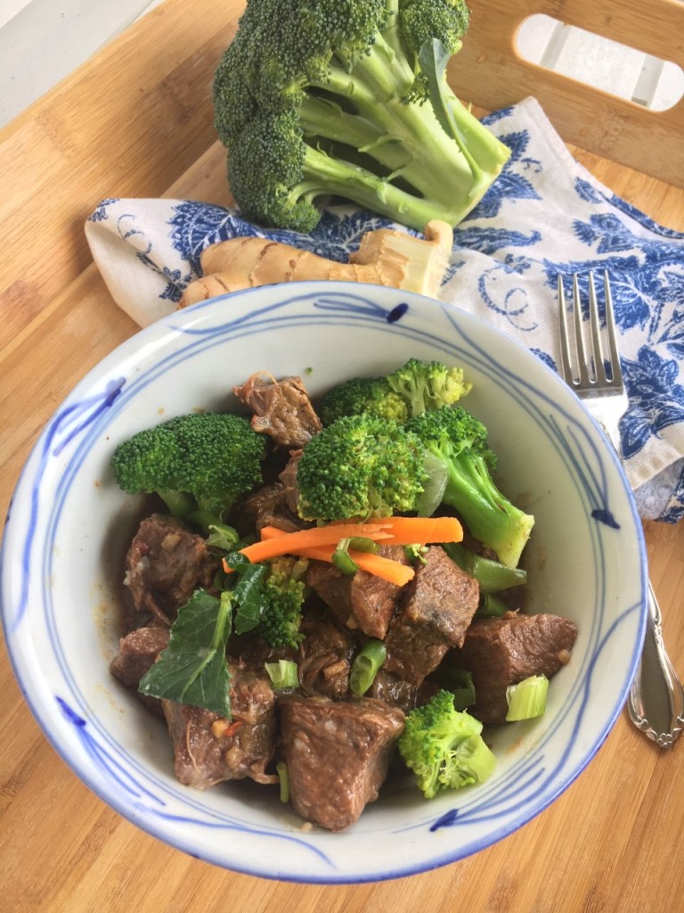A hearty bowl of slow cooker beef and broccoli. Fresh broccoli sprigs in the background.