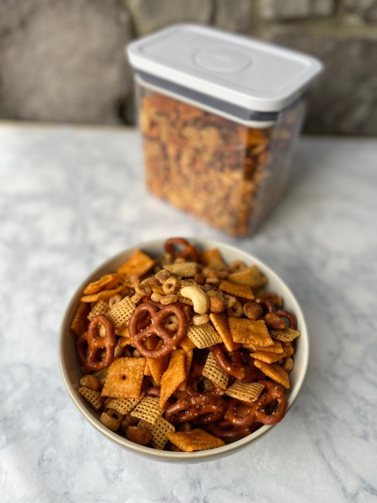 A bowl of homemade Chex mix and a tall storage container in the background.